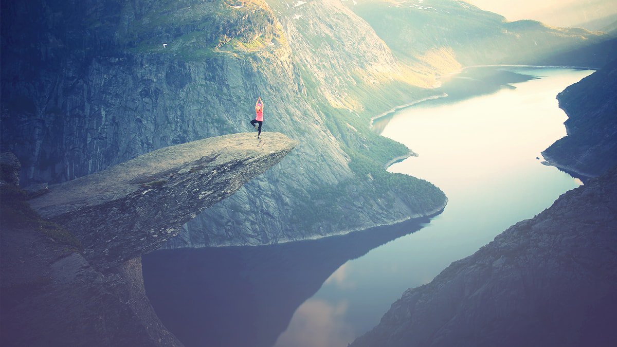 Person doing yoga on a cliff over a lake