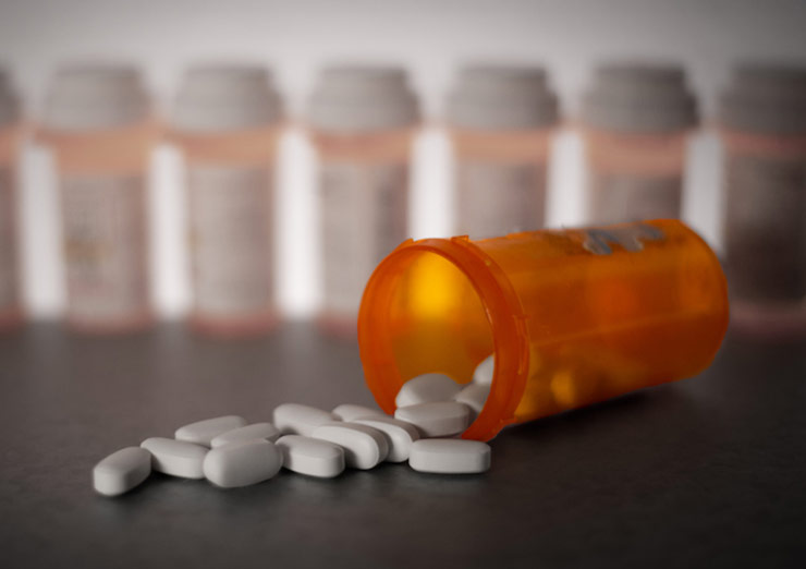 Orange bottle of pills spilled on table with rows of pill bottles in background