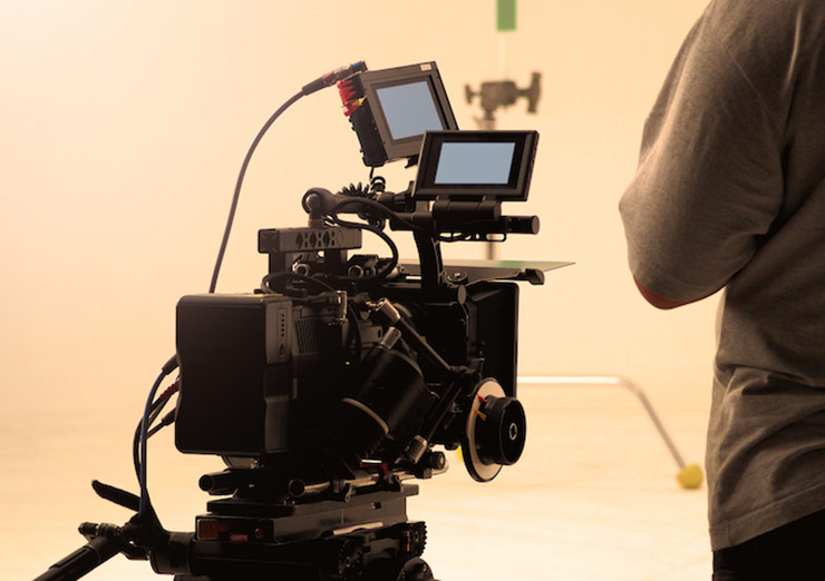 Video camera with person standing to right in studio