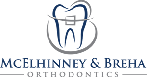 McElhinney and Breha Smiles Logo - Dark blue and gray serif type with tooth icon above
