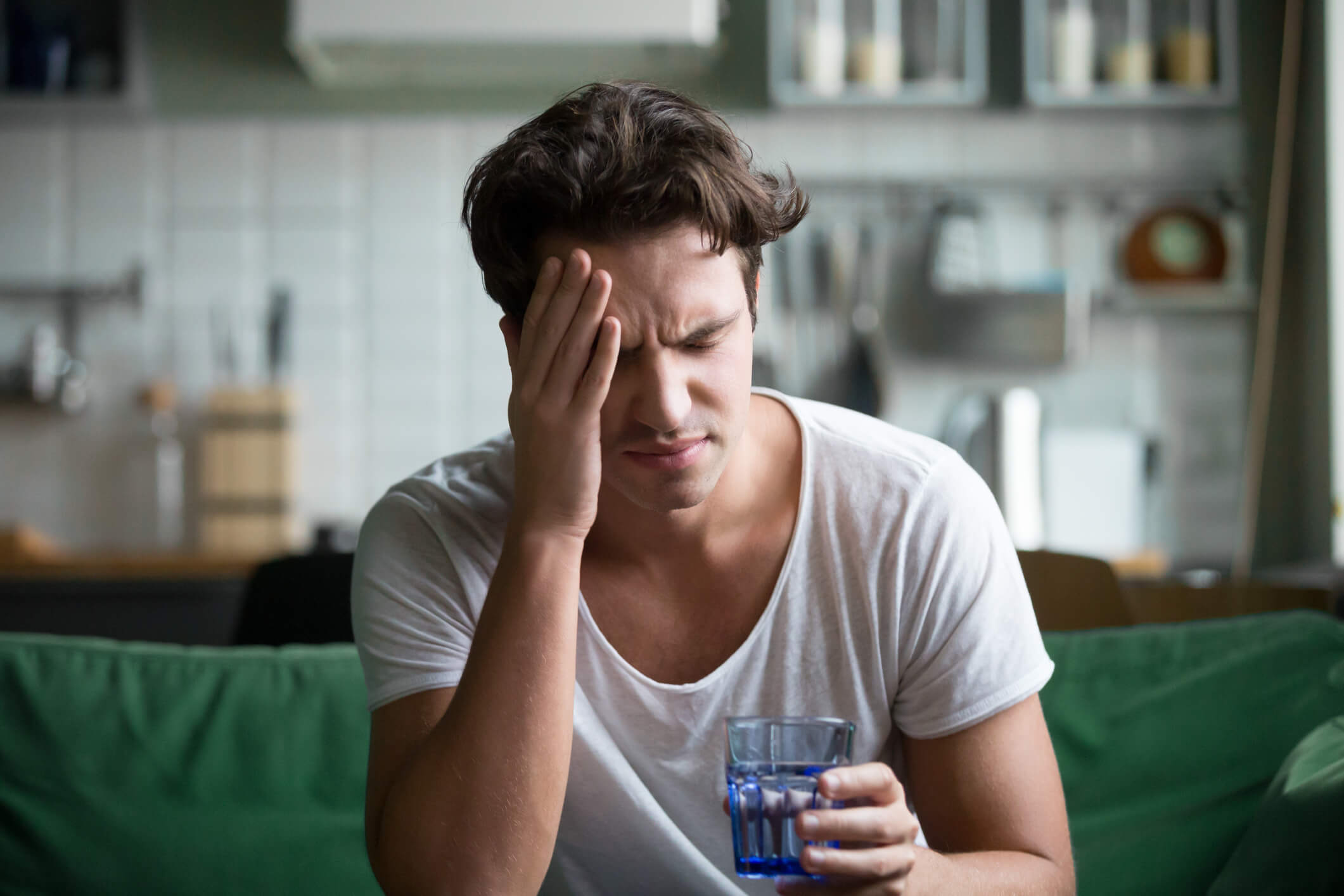 Young man holding his head and a glass of water